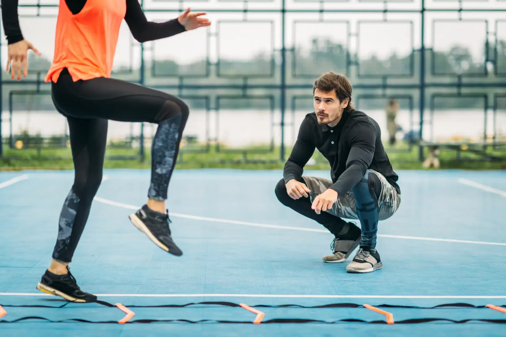 Young woman exercising with personal fitness coach using agility ladder. Agility skill improvement.